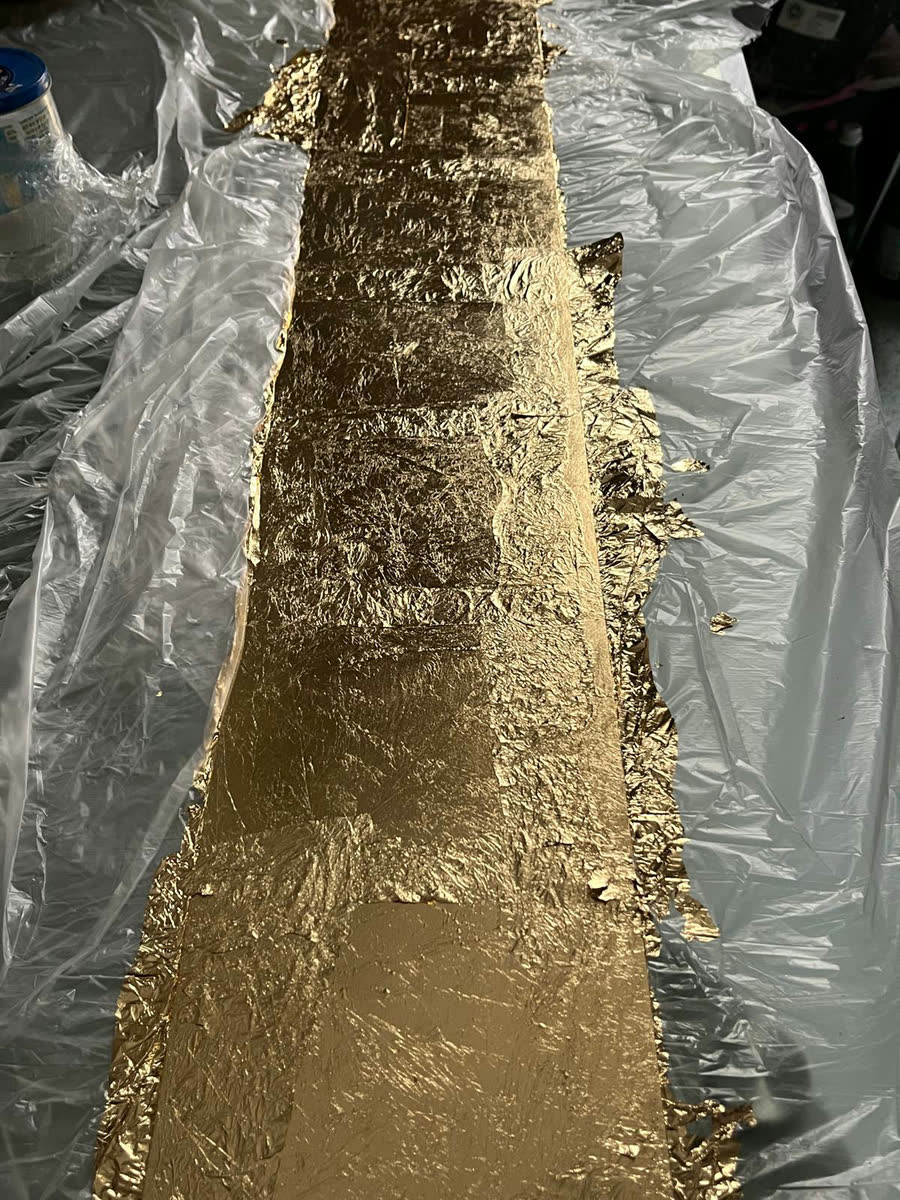Blattgold wird in einzelnen Blättern auf eine Plexiglasfläche aufgezogen, darunter Malerfolie