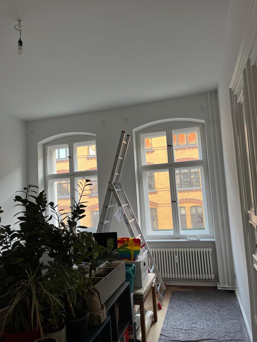 Altbauzimmer vor dem farbigen Anstrich, helle Wände, Leiter und abgedeckte Einrichtung