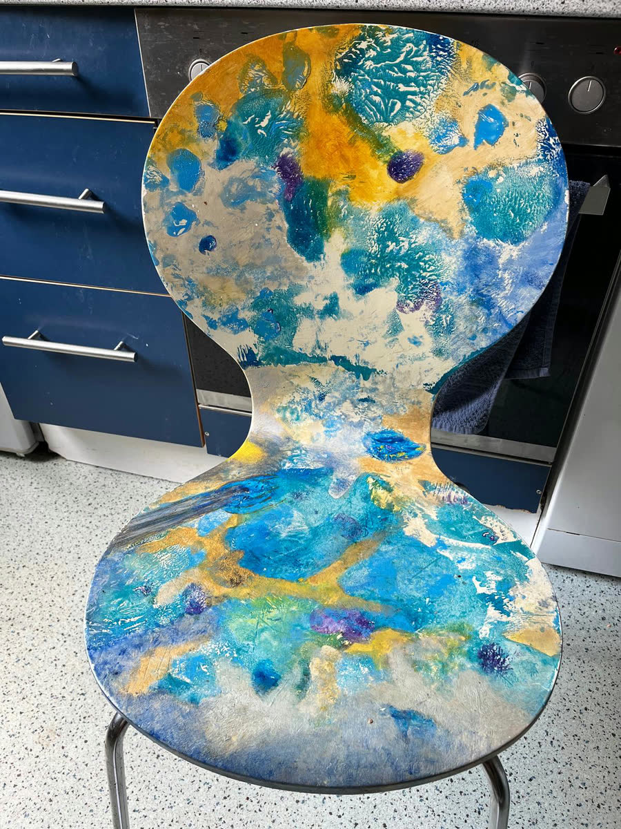 Frei bemalter Holzstuhl mit vielen Farbschichten in Blau, Türkis und Ockergelb
