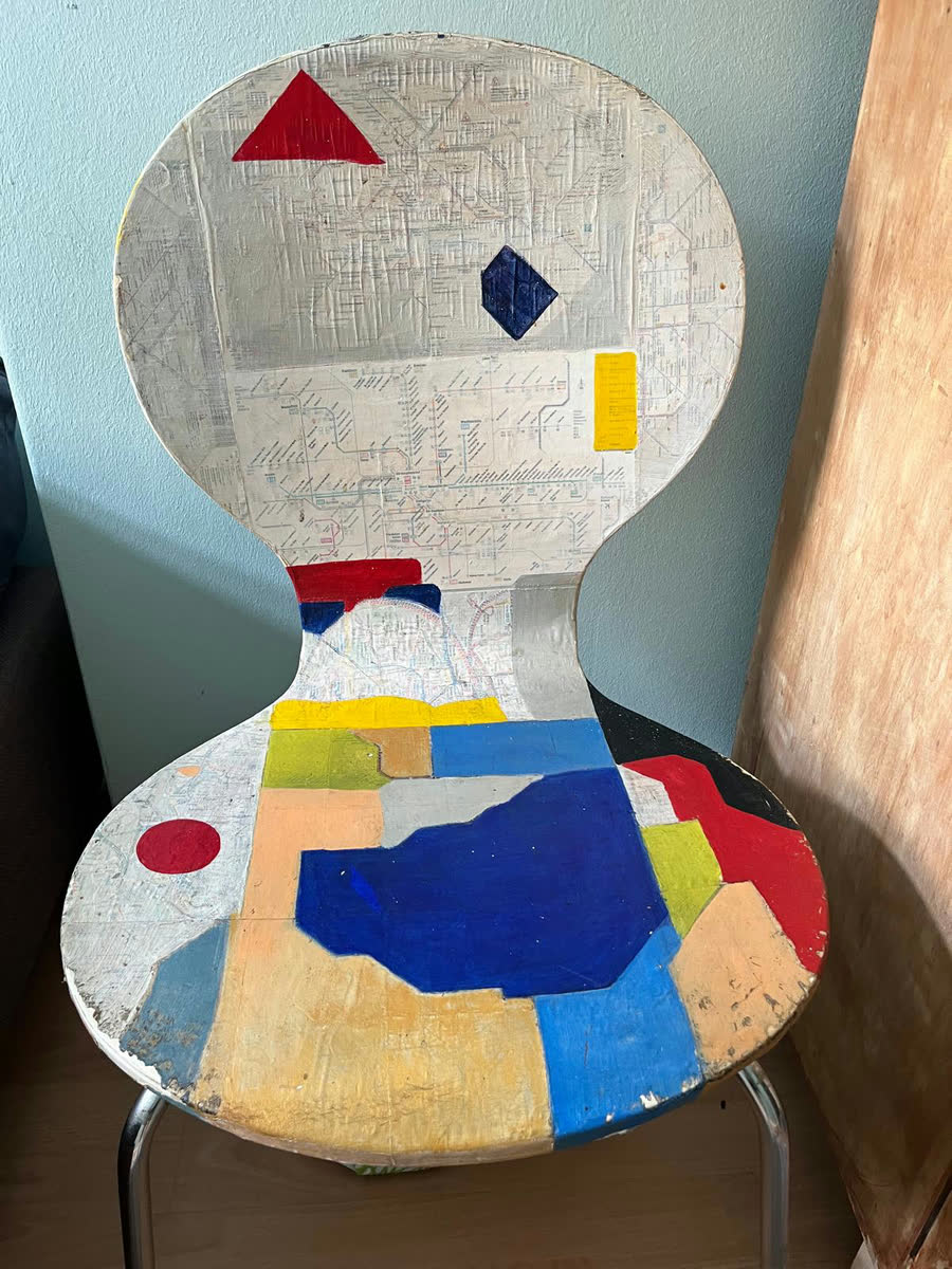 Bemalter Stuhl mit geometrischen Farbflächen in Rot, Blau und Gelb über collagiertem Kartenmaterial