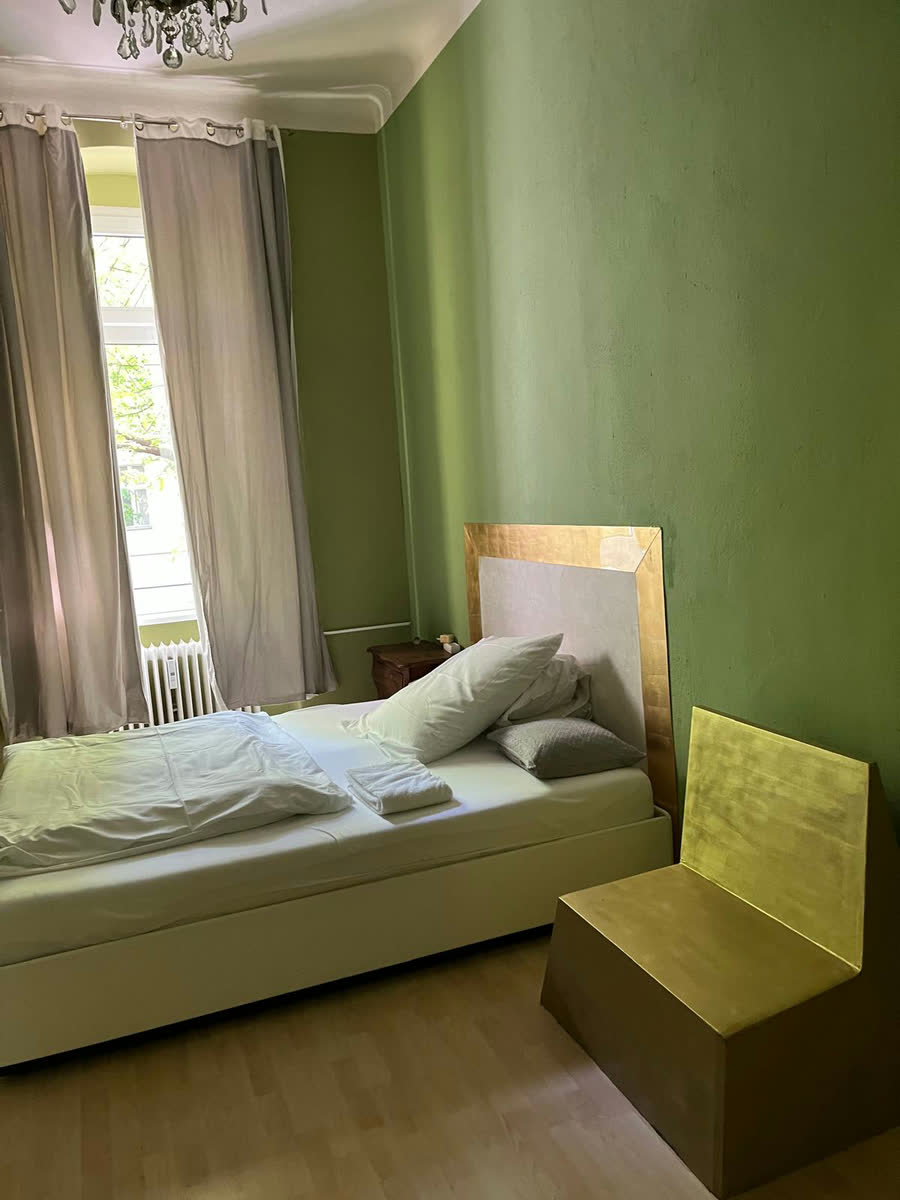 Blick in den grünen Schlafraum mit Bett, vergoldetem Kopfteil und Fenster mit langen Vorhängen