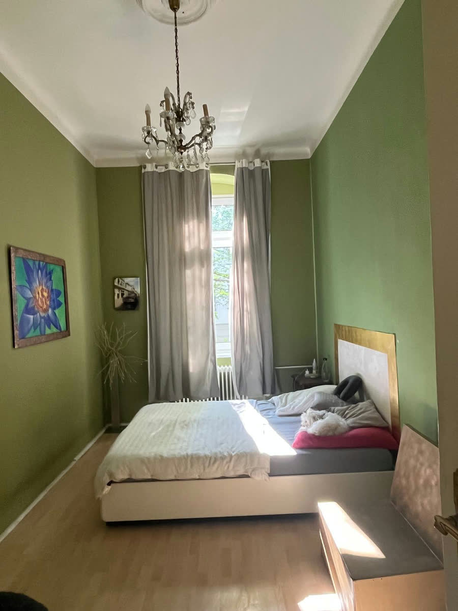Gesamtansicht des Raumes mit hoher Decke, Kristallleuchter und Bildern an der Wand